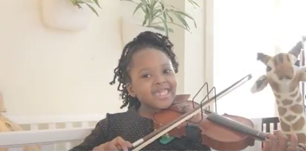 Young girl playing the violin, smiling brightly.