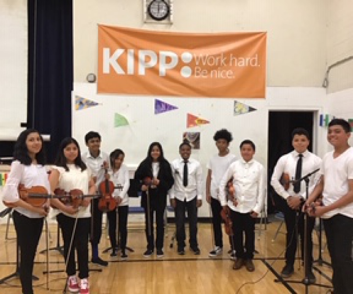 Group of students holding violins at a school event.