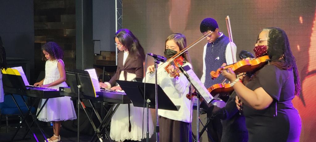 Group performing on stage with violins and keyboards.