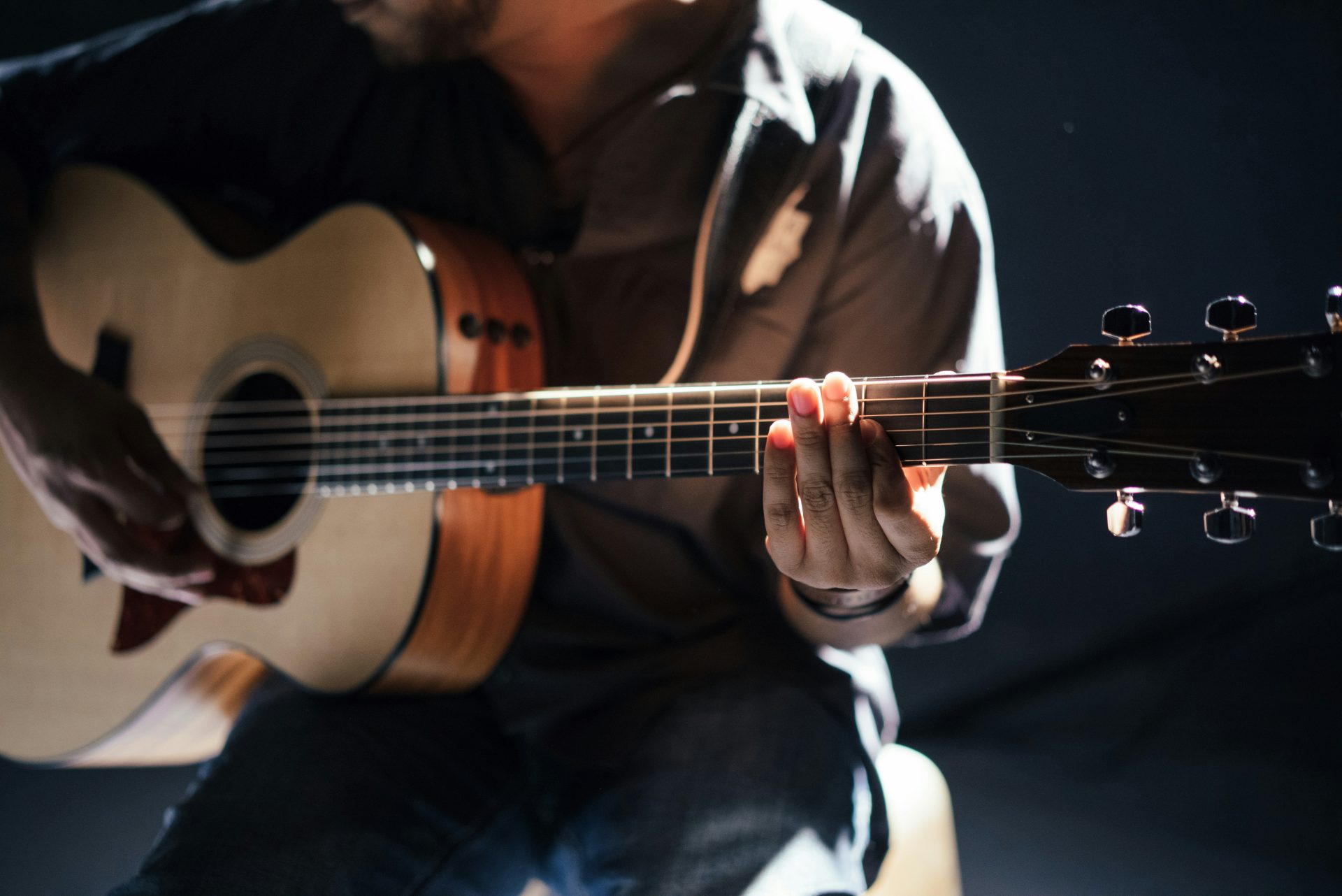 Musician playing an acoustic guitar in dim lighting