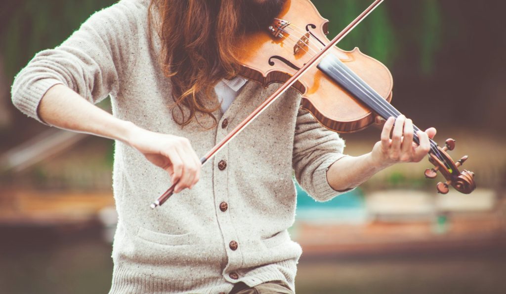 Person playing a violin outdoors, close-up view.