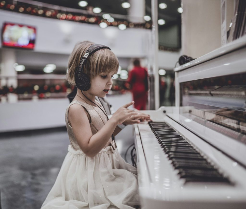 Little girl wearing headphones playing a piano.